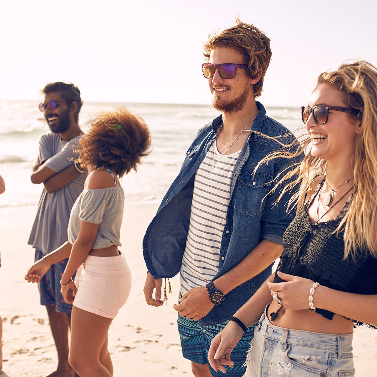 Group of friends walking along a beach at summertime. Happy young people enjoying a day at beach.